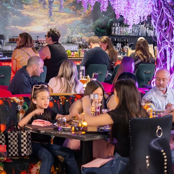 Diners enjoying a vibrant restaurant interior with floral decor, a bar, and colorful seating.