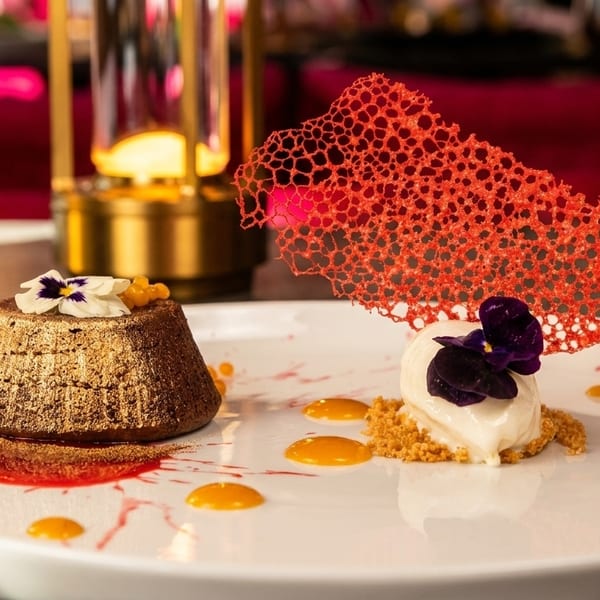 A gold-dusted chocolate lava cake and vanilla ice cream with a red sugar tuile on a white plate.
