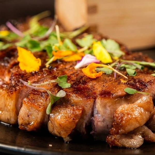 Sliced grilled steak garnished with microgreens and edible flowers on a dark plate.