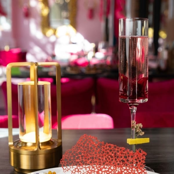 A pink cocktail and a golden lantern on a table in a vibrant pink restaurant setting.