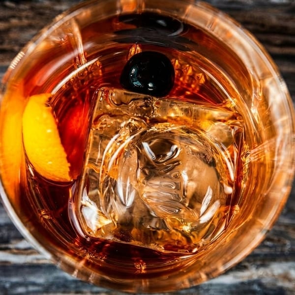 Overhead view of an Old Fashioned cocktail with a cherry, orange peel, and ice.