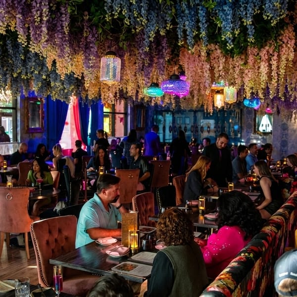 A vibrant restaurant interior with diners, colorful floral ceiling decor, and ornate lighting fixtures.